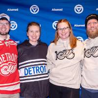 Group of 4 posing for photo, two wearing their custom GVSU Night at the Red Wings sweatshirts